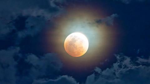 Image of Moon with reddish tinge in cloudy skies