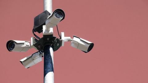 Four CCTV cameras on a pole, in front of a pink background