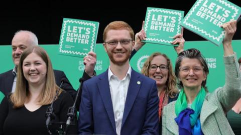 A group shot of smiling Green politicians holding up their election manifesto booklets