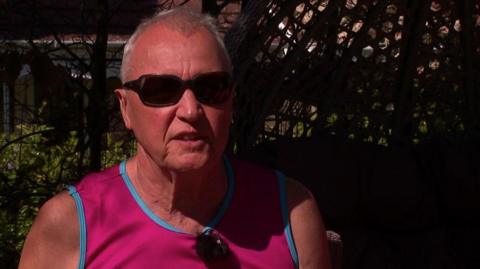 Man with grey hair and glasses. He's wearing a pink vest.