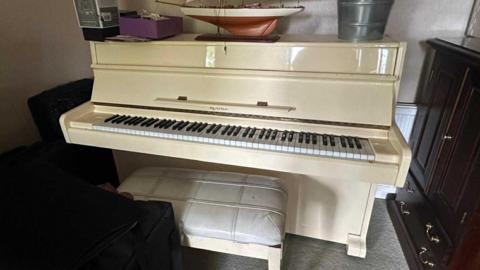 A white piano with a stool and a few items sitting on top of it