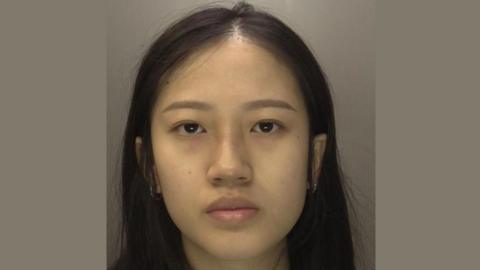 Police mugshot of a young woman with long dark brown hair and hoop earrings.