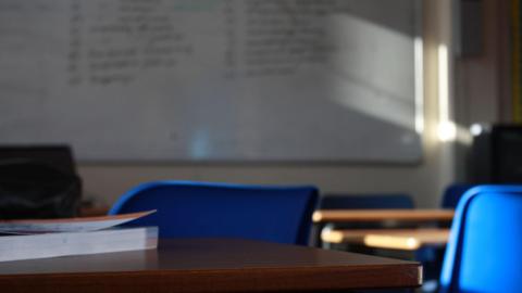 A classroom, with two blue chairs, a whiteboard and a book on a desk