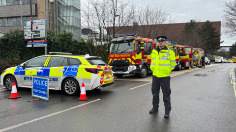 A policeman standing in the road with police cars and a line of fire engines in Coxford Road.