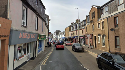 A street with shops on both sides and cars going down the road in both directions 