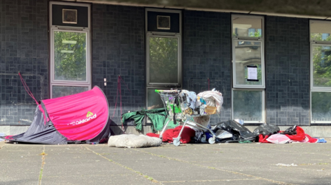 A pink domed tent next to piles of rubbish, including a dumped shopping trolley.
