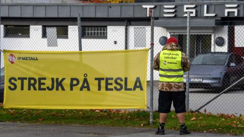 Tesla mechanic Janis Kuzma standing on the picket line outside a Tesla garage in Malmö. His sign says "Strike at Tesla"