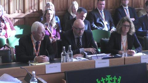 Three people sit at a committee hearing