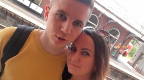 Maksym and his mother Olesia embrace on a platform at Hull Train Station. Both are smiling and wearing yellow tops.  