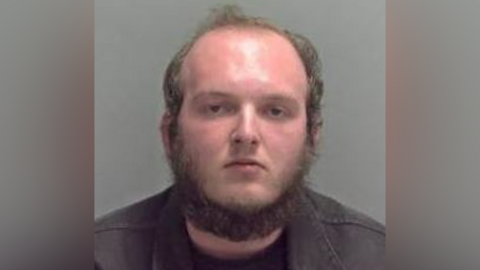 Connor Yaxley appears in his police custody photo, with a beard, receding hairline and dark coloured jacket. 