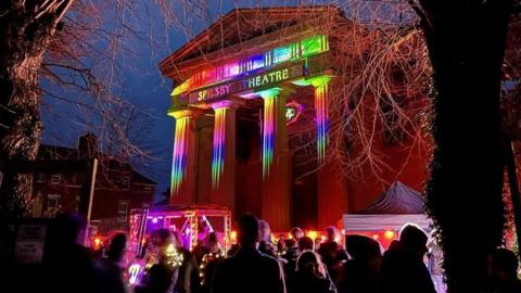 Columns of Spilsby Thearte illuminated with brightly-coloured lights with spectators looking on