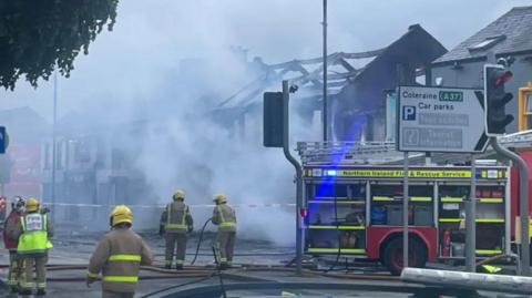 Firefighters pictured beside a fire engine  scene in front of the smoke-filled remains of the former nightclub in Catherine Street