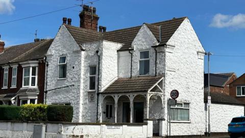 Semi-detached house on corner of street with white jagged walls and a brown roof