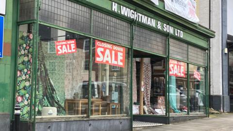 Facade of shop with red signs on windows reading "Closing Down Sale'"