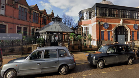 A street with black taxi cabs outside a red-bricked building, which has signs that read "42".