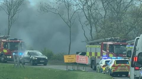 A road side image of black smoke in the air, and emergency service vehicles in Sutton. 