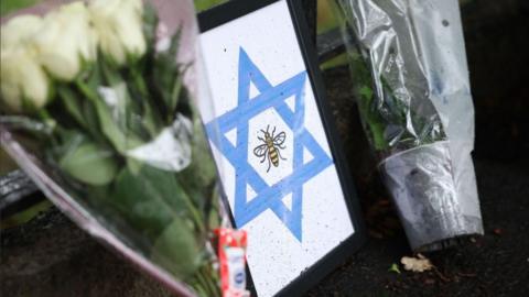 A framed Star of David with a bee, the symbol of Manchester, is left at the scene of a deadly terror attack in Manchester. Bunches of flowers have also been left on either side of the picture.