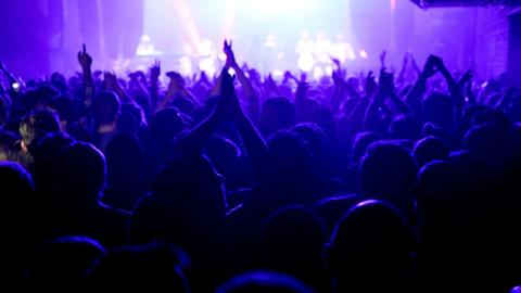 A picture taken behind the crowd at Warehouse project in Manchester with their hands in the air looking towards the stage.