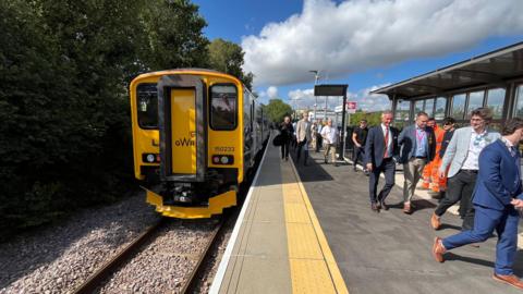 A yellow GWR train at a platform. There are people walking towards the camera on the right.