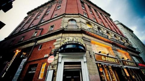 An image of the Epstein Theatre with the camera at a low angle looking up at the building. The door in on the corner of the theatre and the name of it is written in art deco-style signage above. Stonework around the entrance eventually leads into red brick.