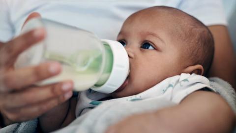 Stock photo shows a baby being held and fed with a formula milk bottle.