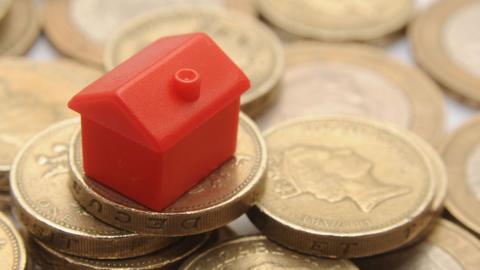 A small red plastic house on top of a pile of £1 coins.