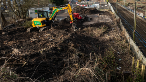 A railway line with construction work being carried out alongside involving a yellow mechanical digger