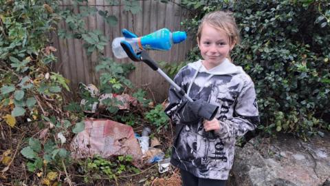 Image of nine year old Theo out picking up litter using a pair of grabbers to hold up an empty plastic bottle