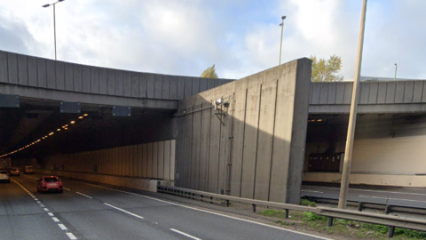 A red car drives into the Hatfield Tunnel, on a cloudy day. 