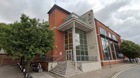Hereford Magistrates Court is pictured with stone steps leading up to an entrance made up of concrete and glass. The rest of the exterior is red brick. 