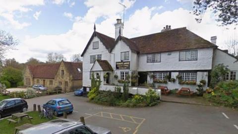 A 16th Century pub. There are cars parked outside the white building.
