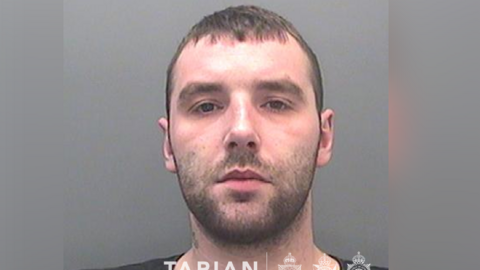 A custody image of David Braddon. He has dark stubble and looks at the camera with a neutral expression. 