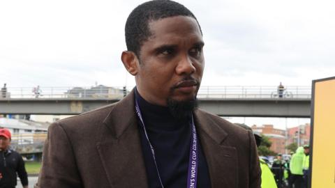 An image of Samuel Eto'o, wearing a black polo neck jumper and a brown jacket, arriving at a football match in September 2024