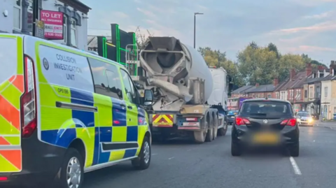 A police collision investigation van parked behind a cement mixer lorry on a city street