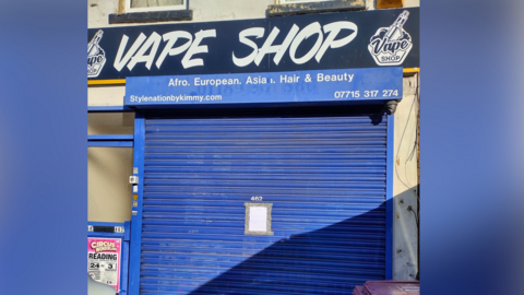 A shopfront that has blue shutters and a blue sign that says "Vape Shop".