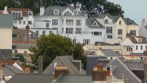 Rows of homes in one area in Guernsey, with trees and blue skies behind.