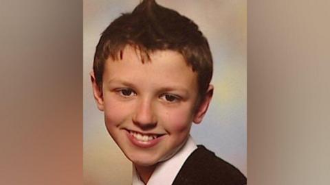 Oliver King has short brown hair and is wearing a white shirt and a dark-coloured top. He is smiling at the camera.