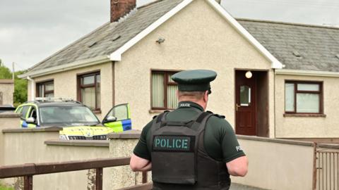 A police officer and a police car outside Michael McConville's home on Annaghmare Road in Crossmaglen in June 2024.   