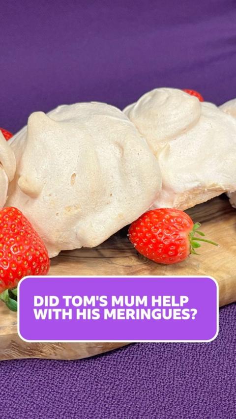 A close up of white circular meringues, with strawberries scattered around them on a wooden board and purple background