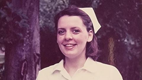 A vintage sepia picture of a young nurse, who is wearing a nurse's hat and standing in front of some trees.