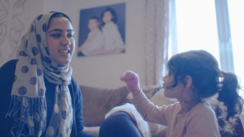 A mother and daughter playing with a sock puppet in the living room.