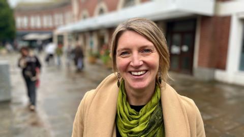 Nicola Wheeler, chief executive of Exeter's business improvement district, InExeter, wearing a green scarf and a beige coat standing on the pavement outside Exeter Central station