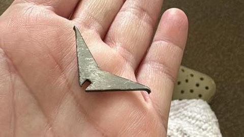 A hand holding a metallic spike which look like a boomerang with sharper edges.