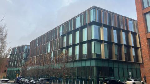 An exterior shot of West Northamptonshire Council's building. It is a modern three-storey structure with floor-to-ceiling windows on each storey.