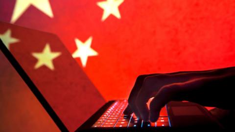 hands in shadow typing on a computer in front of a Chinese flag