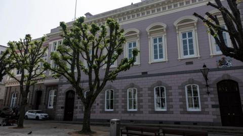 The States Building in St Helier, with trees and benches in the foreground on a sunny day.