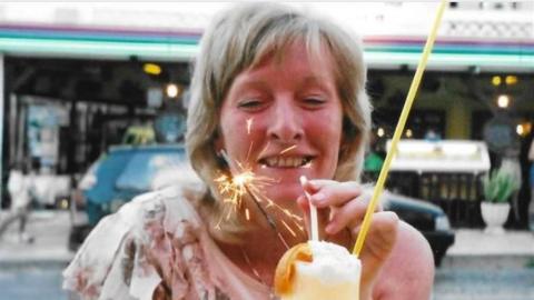 Annette Smith about to sip a cocktail through a straw, with a street behind her suggesting she is outside a cafe