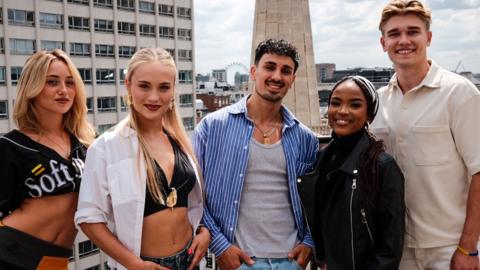 Five young people - three females and one male - stand on a rooftop in central London.