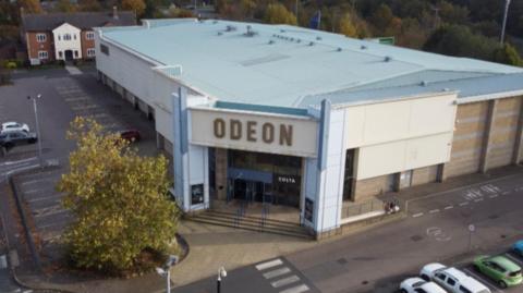 A drone shot of the Odeon building with cars parked outside.