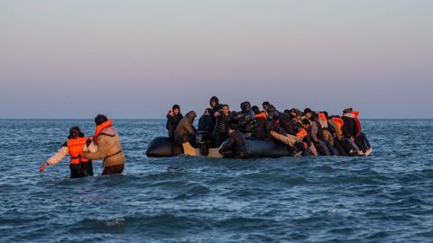 A woman is helped to board a migrant dinghy with other people on board into the English Channel in 2026 in Gravelines, France. 